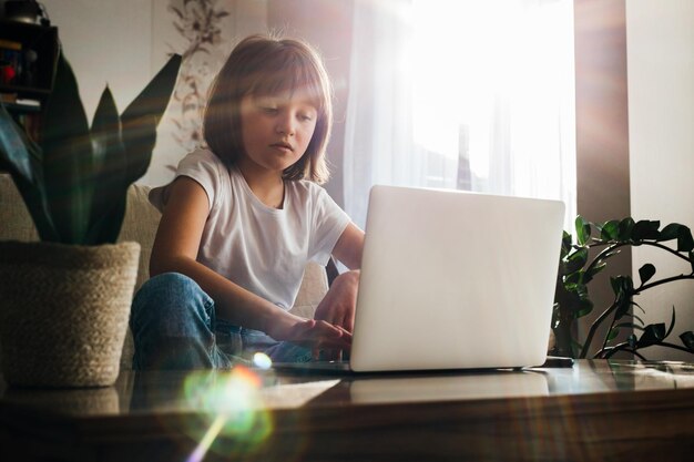 Aprendizagem à distância a menina senta-se em casa no sofá e estuda usando um laptop ou faz chamadas