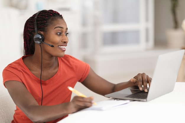 Aprendizagem à distância mulher negra no fone de ouvido estudo on-line com laptop em casa