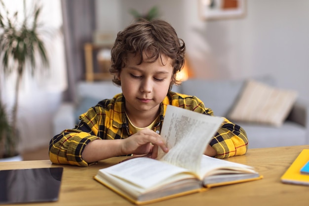 Aprendizagem doméstica Menino bonitinho estuda para ler o livro de leitura na mesa estudando em casa espaço livre
