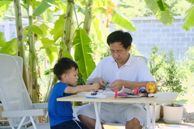 Aprendizaje basado en el hogar (HBL), padres sentados, educación en el hogar con un niño pequeño, padre e hijo asiáticos que se divierten haciendo fáciles botes de juguete STEM para estudiantes en casa, juguetes educativos para niños pequeños