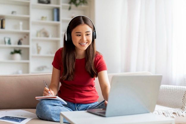 Aprendizaje a distancia mujer asiática sonriente con auriculares estudiando con computadora portátil en casa