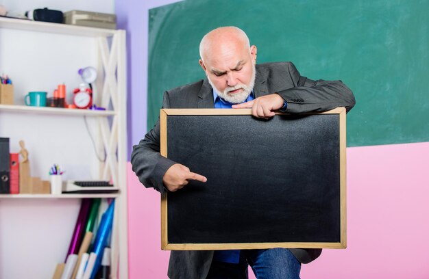 Foto apresentação professor sênior com informações de quadro-negro vazio está aqui lugar de resultados de exame e graduação para espaço de cópia homem professor maduro segura quadro de giz de volta à escola conceito de educação