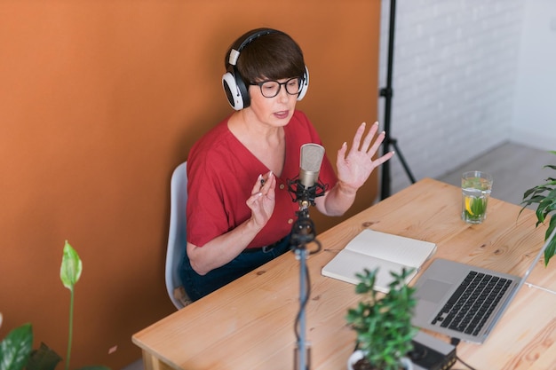 Apresentadora de rádio feminina de meia-idade falando no microfone e lendo a transmissão de rádio de notícias