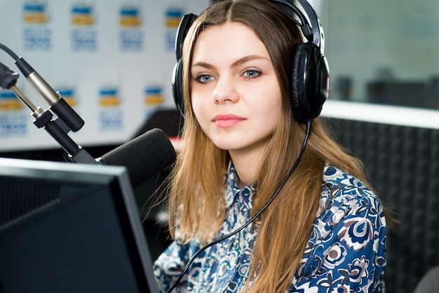 Apresentadora de rádio jovem e bonita sentada no estúdio com fones de ouvido e falando no ar