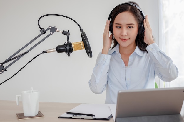 Apresentadora de rádio linda jovem asiática trabalhando, configurando o microfone, preparando-se para falar antes de gravar o podcast e ao vivo nas mídias sociais. Tecnologia do on-air online na transmissão em home studio.