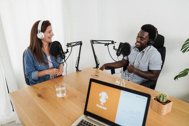 Apresentadores multirraciais transmitindo podcast juntos em estúdio doméstico - foco no rosto da mulher