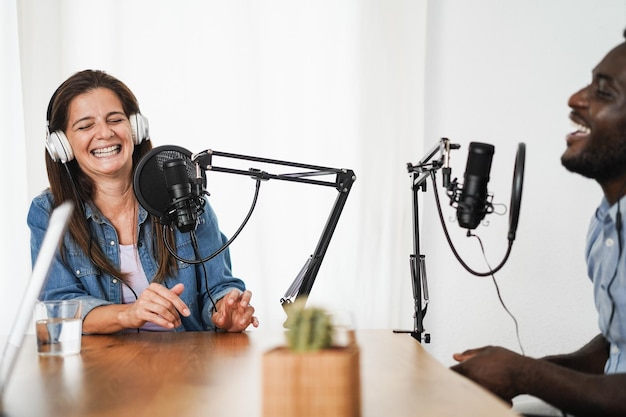 Apresentadores multirraciais transmitindo podcast juntos em estúdio doméstico - foco no rosto da mulher