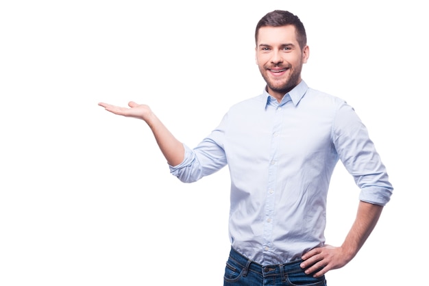 Apresentando novo projeto. jovem bonito com uma camisa, olhando para a câmera e segurando o espaço da cópia em pé contra um fundo branco