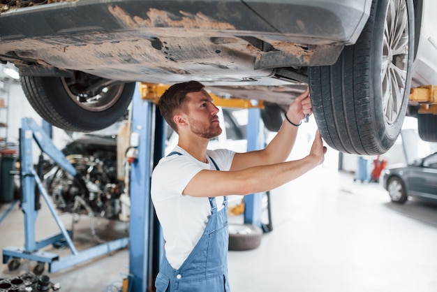 Apretando algunos tornillos. Empleado en el uniforme de color azul trabaja en el salón del automóvil