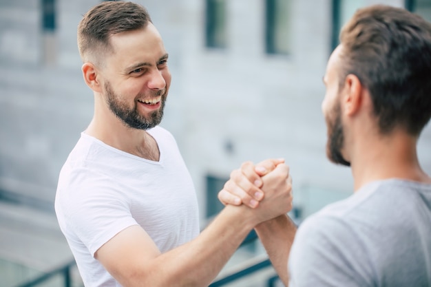 Foto apretón de manos amistoso de hombres. dos jóvenes amigos guapos barbudos en camisetas casuales están posando juntos