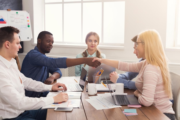 Apretón de manos multiétnico de negocios en la reunión corporativa de la oficina, celebración de contrato y concepto de acuerdo exitoso. Manos de hombre de negocios alegre y empresaria se encuentran, espacio de copia