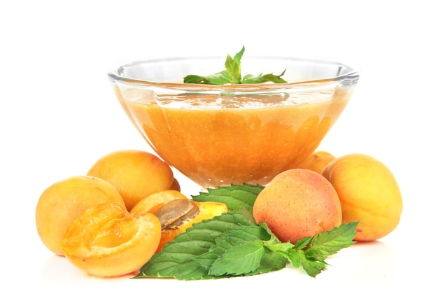 Aprikosenmarmelade in Glasschüssel und frischen Aprikosen, isoliert auf weiss