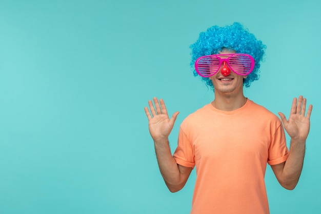 Aprilscherztag Typ lächelnd abgestreift rosa Sonnenbrille rote Nase blaues Haar Clown Kostüm lustige Hände hoch