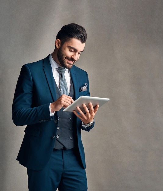 Aprovechado las últimas tendencias corporativas Foto de estudio de un joven hombre de negocios elegantemente vestido usando una tableta digital contra un fondo gris