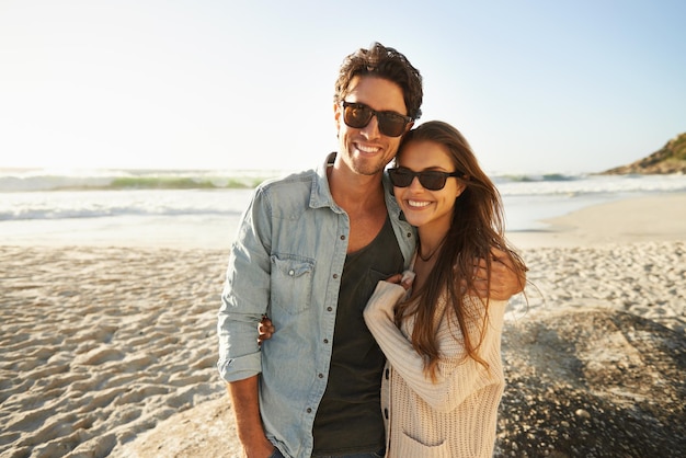 Aproveitando a brisa do mar e o sol Foto de um lindo casal jovem lado a lado na praia