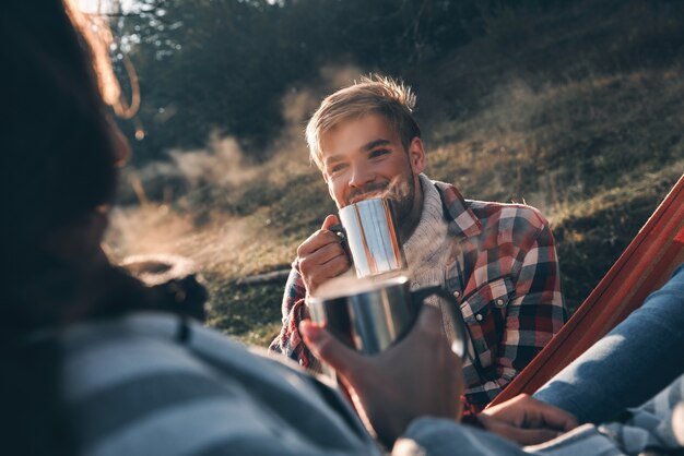 Aproveitando o café quente. Jovem casal feliz tomando café da manhã enquanto acampa nas montanhas