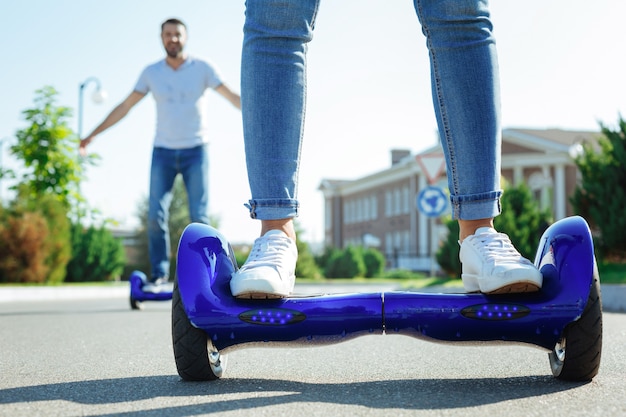 Aproveitando o passeio. O close up de pernas femininas em jeans de pé em uma prancha azul enquanto um homem alegre cavalgando na mesma ao fundo