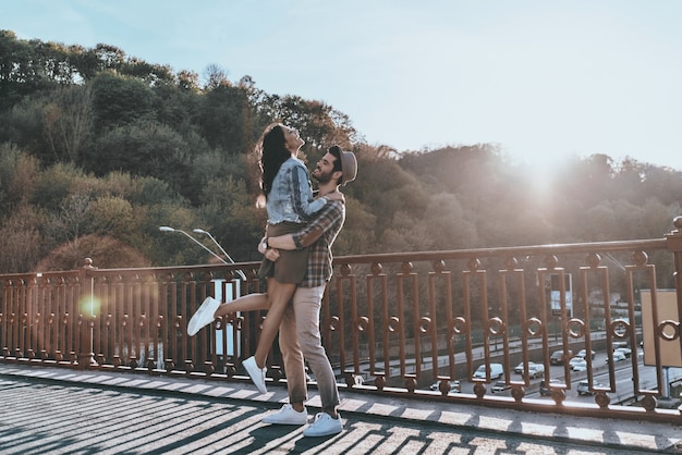 Aproveitando o pôr do sol juntos. Comprimento total de um homem bonito carregando uma mulher jovem e atraente