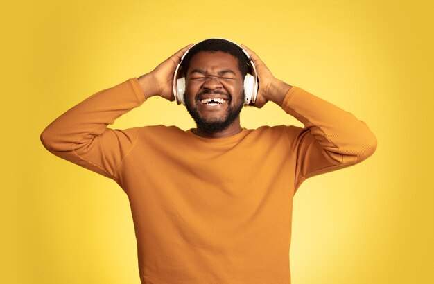 Aproveitando o retrato de jovem afro-americano isolado na expressão facial de fundo amarelo do estúdio