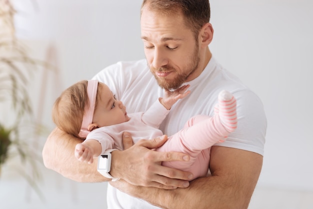 Aproveitando o tempo com meu bebê. Pai barbudo carismático e alegre em casa, segurando a menina nos braços enquanto expressa amor e carinho