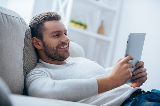 Aproveitando o tempo em casa. Jovem alegre segurando um tablet digital e parecendo relaxado