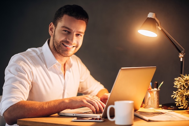 Aproveitando seu trabalho mesmo à noite. Jovem confiante e sorridente