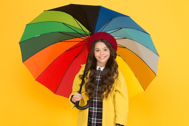 Aproveite o conceito de chuva Garota de criança feliz segure guarda-chuva colorido de arco-íris Tempo chuvoso com roupas adequadas Guarda-chuva brilhante Divirta-se conceito de positividade Diversão em dia chuvoso Passeio feliz sob o guarda-chuva