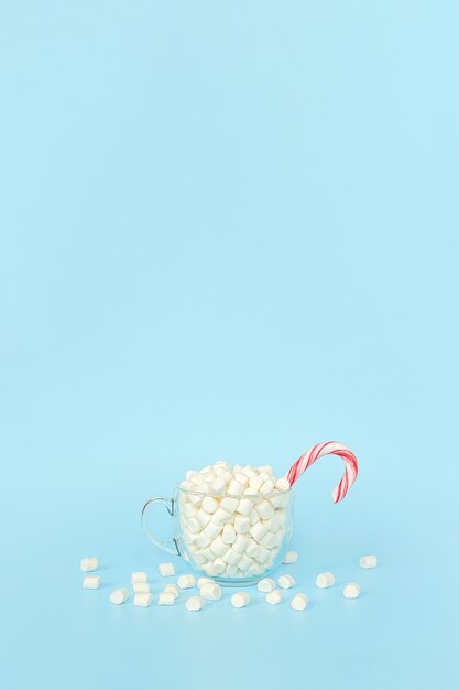 Aproveite o inverno, cartão postal. Grande copo transparente de marshmallows com bengala de pirulito vermelho sobre fundo azul.