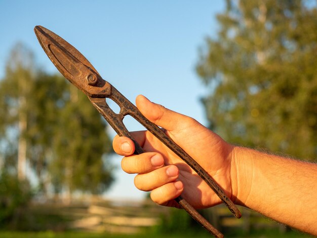 Aproximação da mão de um homem segurando uma velha tesoura de metal enferrujada Fundo desfocado