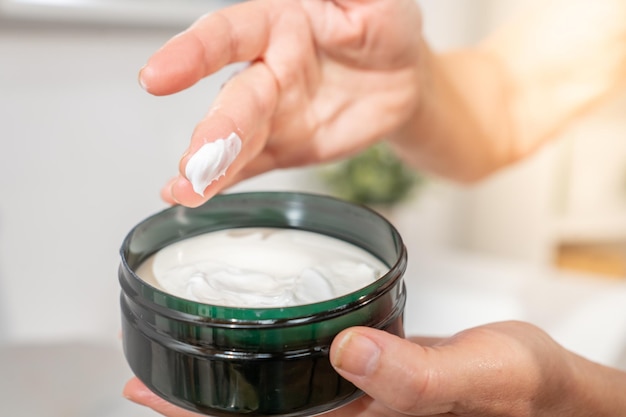 Aproximação da mão de uma mulher de meia-idade manchando o dedo com creme cosmético para cuidados com a pele e beleza