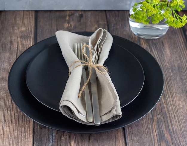 Aproximação da mesa com talheres de prata de placa preta e guardanapo de linho na mesa de madeira Cenário de jantar