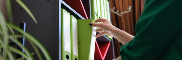 Foto aproximação da mulher tirando a documentação e contabilidade do trabalho do escritório da pasta de papel verde da prateleira