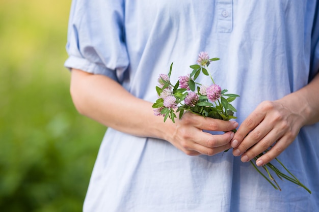 Aproximação das mãos de uma jovem segurando flores silvestres Garota se divertindo e aproveitando o sol no parque Verão