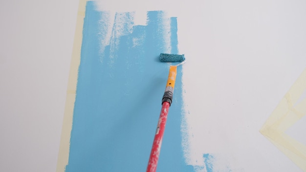Aproximação das paredes de pintura do decorador em cor azul clara com decoração interior de rolos ou