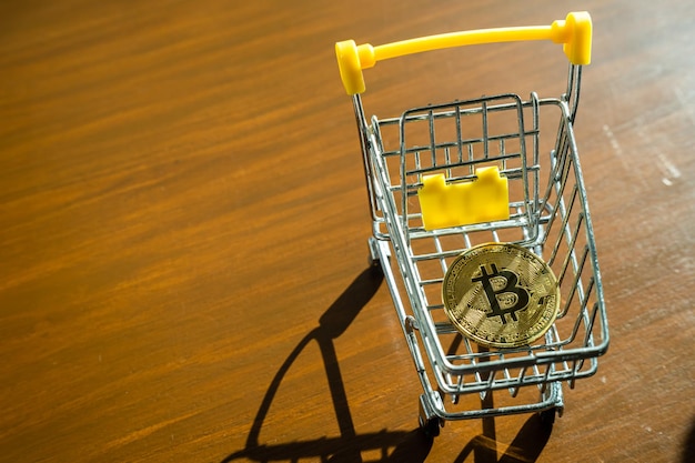 Aproximação de bitcoins dourados ou moedas de criptomoeda ou símbolos no carrinho de compras na mesa Conceito de moeda futura