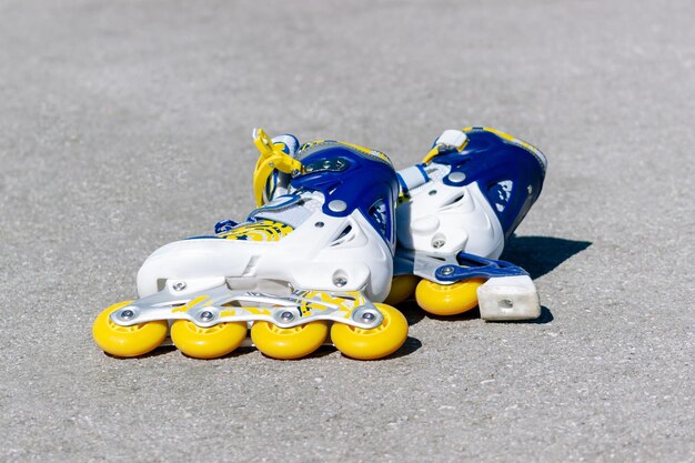 Aproximação de botas de patinação infantil amarelas azuis no asfalto Aprendendo a andar de patins