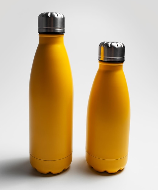 Aproximação de grandes e pequenas garrafas de água ecológicas reutilizáveis amarelas em fundo cinza