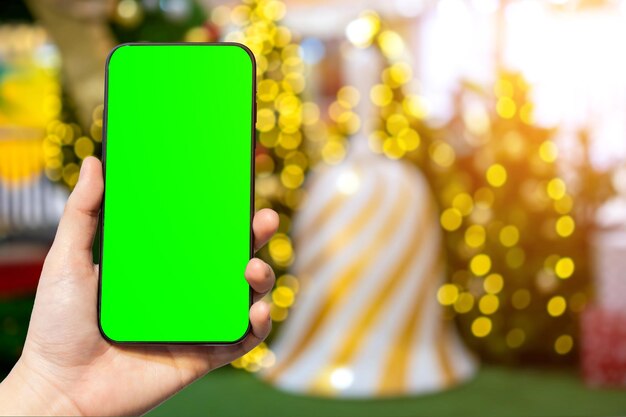 Aproximação de imagens desfocadas do smartphone de uso feminino com bolas coloridas na decoração verde do fundo da árvore de Natal durante o Natal e o Ano Novo Tela verde