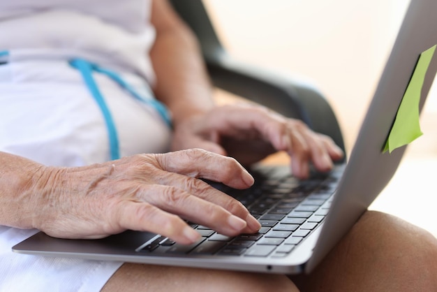 Aproximação de mãos femininas idosas digitando no laptop moderno mulher idosa trabalhando remotamente on-line