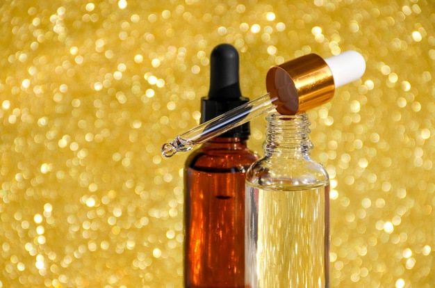 Aproximação de soro em garrafas de vidro sobre fundo dourado Cosméticos e cuidados