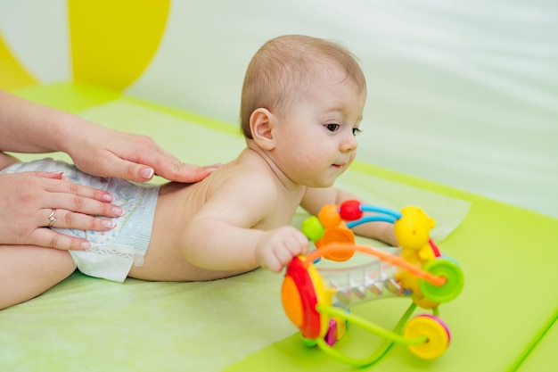 Aproximação de um bebê na clínica Paciente bonito Criança feliz está deitada na barriga perto de um brinquedo bonito e brilhante