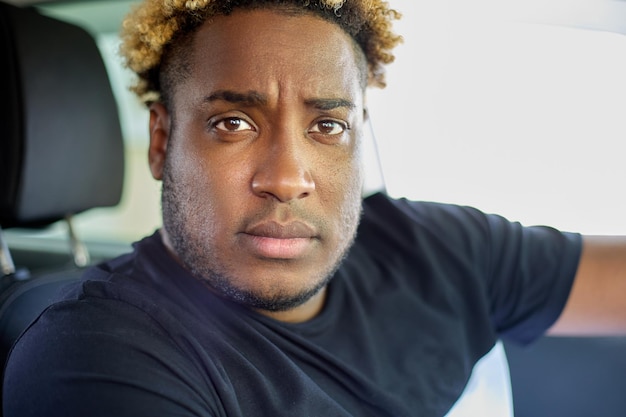 Aproximação de um homem afro-americano sério e confiante em uma camiseta sentada em seu carro