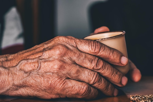 Aproximação de um idoso irreconhecível com rugas e veias segurando uma caneca de café quente