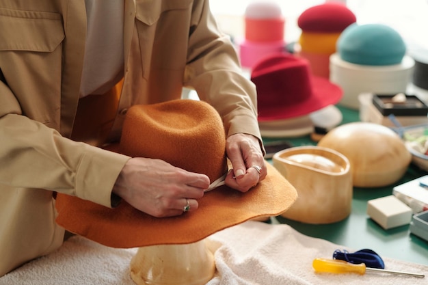 Aproximação de uma jovem artesã criativa consertando o cadarço decorativo ao redor do chapéu