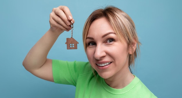 Aproximação de uma loira alegre e feliz com um visual casual que se mostra comprando uma casa em um azul