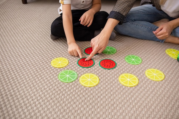 Foto aproximação de uma mãe caucasiana com uma criança jogando cartas de jogos educacionais no tapete da sala