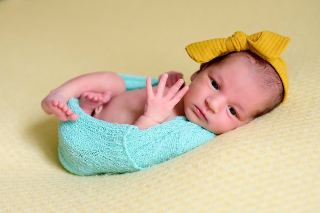 Aproximação de uma menina recém-nascida dentro de uma bola de lã azul sobre um cobertor amarelo com um laço amarelo na cabeça