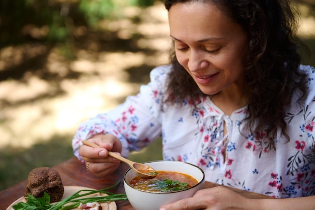 Aproximação de uma mulher encantadora comendo uma deliciosa sopa tradicional de beterraba borscht ucraniana ao ar livre, cozinha eslava