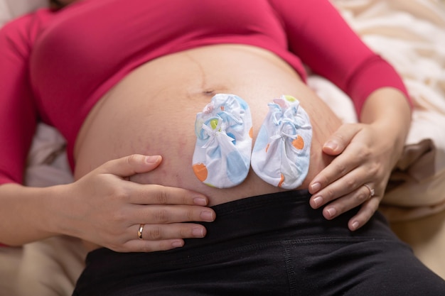 Aproximação de uma mulher grávida na barriga grande com sapatos de criança pequena Conceito de gravidez e bebê esperando