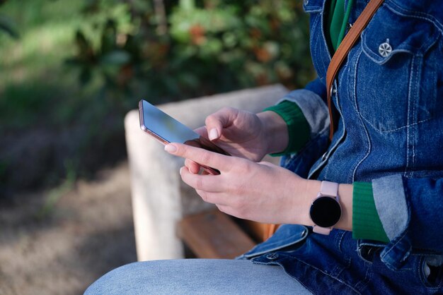 Aproximação de uma mulher relaxando no parque e navegando na internet em um relógio inteligente estiloso de smartphone moderno